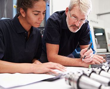 Information For Employees is depicting and image of a student or apprentice leaning over some schematic with her mentor doing the same next to her while he is pointing at an area on the paperwork with his pen, perfect snapshot of 'on the job training'.