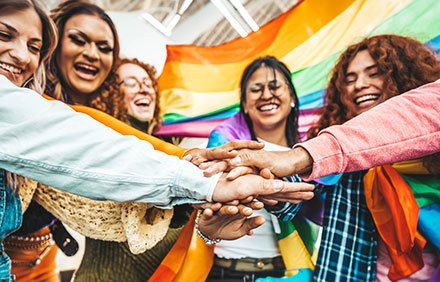 Lgbt group of people stacking hands outside - Diverse happy friends hugging outdoors - Gay pride concept with crowd of guys and girls standing together on city street