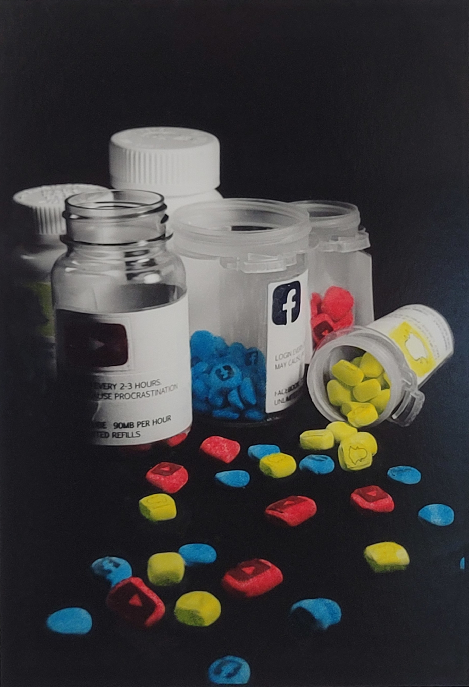 A still life black and white photo. Pill bottles sit with pills strewn across the table, the pills have the social media logos of Facebook, Youtube, and Snapchat. The pills are also colored to match the signature color of each social media platform, Blue, Red, and Yellow
