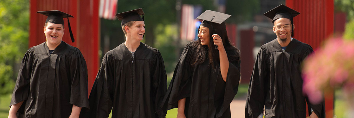 Group of 4 graduates walking and smiling at each other.