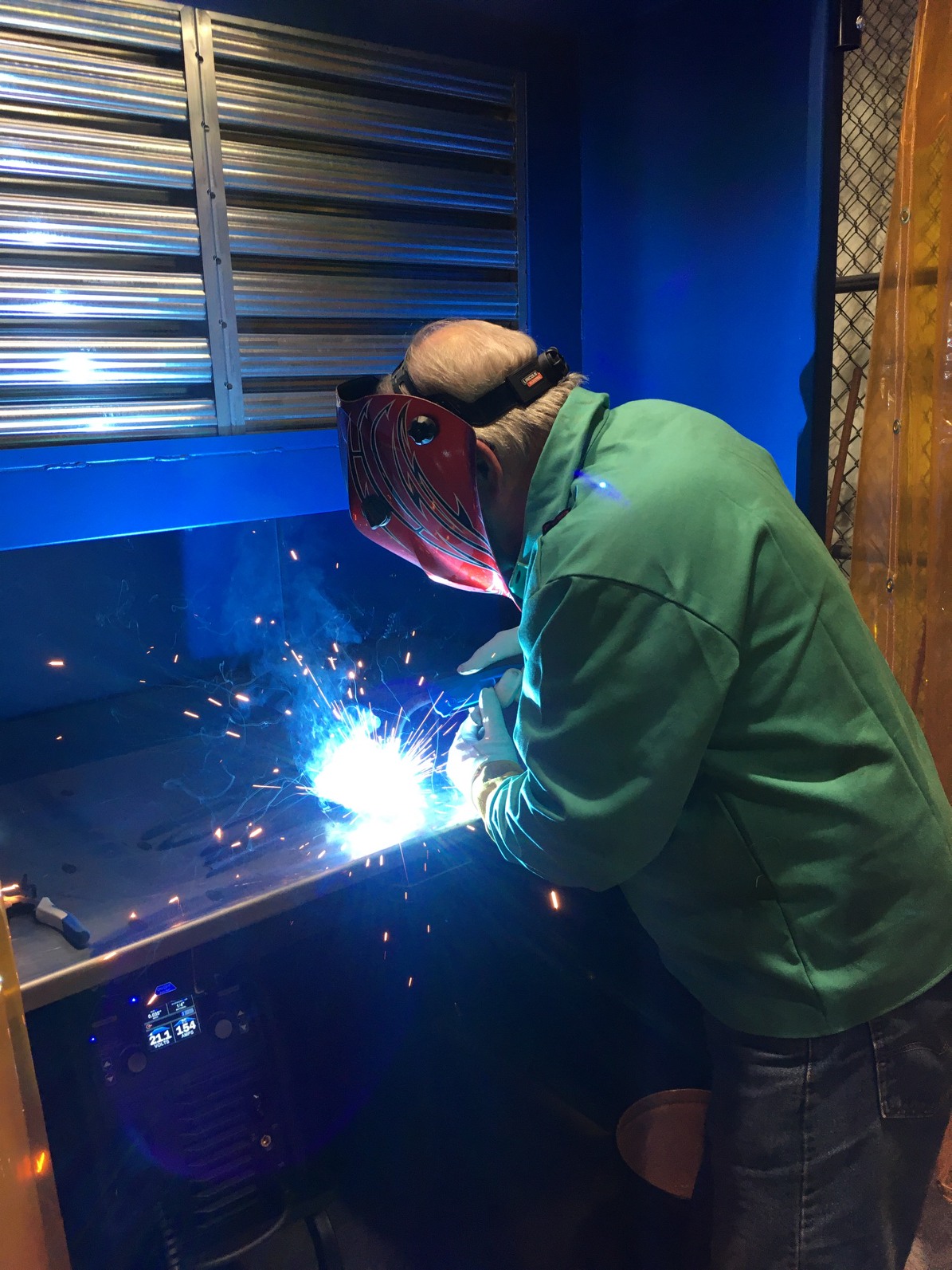Man with helmet and face shield welding in a booth, with sparks flying.