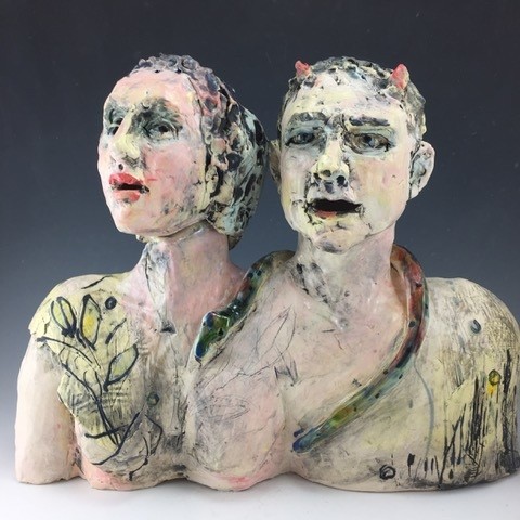 A clay sculpture of two figures, Adam and Eve. Thye are shown connected, their shoulders blended into the other and from the bust up. A snake is draped around Adam’s neck. There is mark making on the forms and a loose, expressionistic feel to the work. Adam has two, small red horns. 