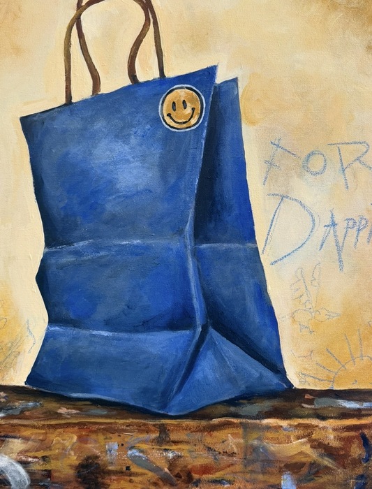 A blue paper bag sits on a wooden surface that is covered by paint marks. A smiley face sticker is on the upper right side of the bag's front. A yellow background has blue scribbled text saying "For Dapp" and childlike drawings drawn on the wall.