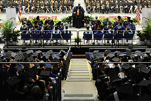 Sinclair faculty seated in the UD Arena bleachers behind the stage of the Graduation ceremony.
