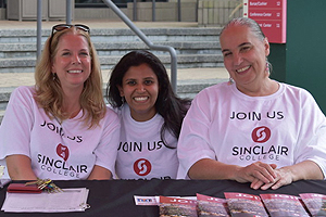 3 Female Sinclair staff sitting at a Welcome week station table handing out packets.