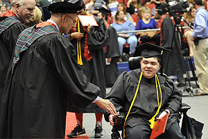 Sinclair student in a wheelchair graduating and shaking the hand of a faculty.
