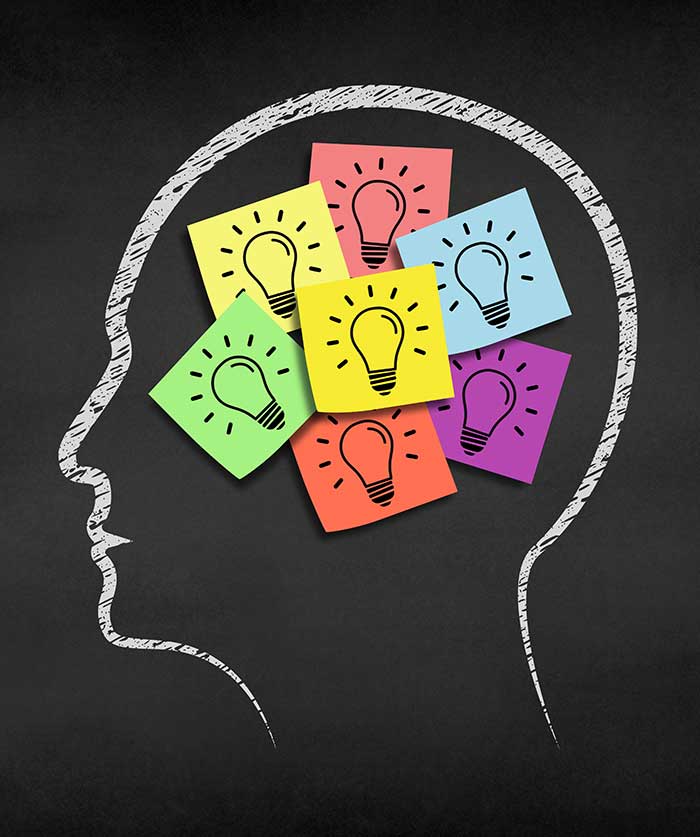 Silhouette of a head with multicolored sticky notes and a lightbulb drawing inside, representing creative thinking.